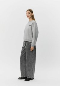 Sivá bavlnená mikina s výšivkou "oui"; má voľný strih a rebrované manžety. Kombinovaná s čiernymi džínsami s vysokým pásom a širokými nohavicami.