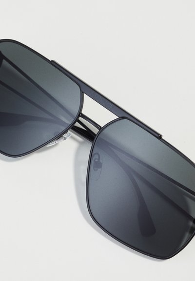 Lunettes de soleil noires rectangulaires avec des verres gris dégradés, monture en métal et plaquettes de nez en silicone transparent, arborant le logo Versace sur la branche.