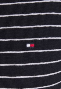Pull en tricot présentant des rayures bleu marine et blanches, avec un petit logo brodé en rouge, blanc et bleu près du centre.
