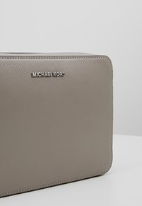 Bolso de mano de cuero texturizado gris con forma rectangular. Presenta accesorios de plata y el logo "MICHAEL KORS" en la parte frontal.