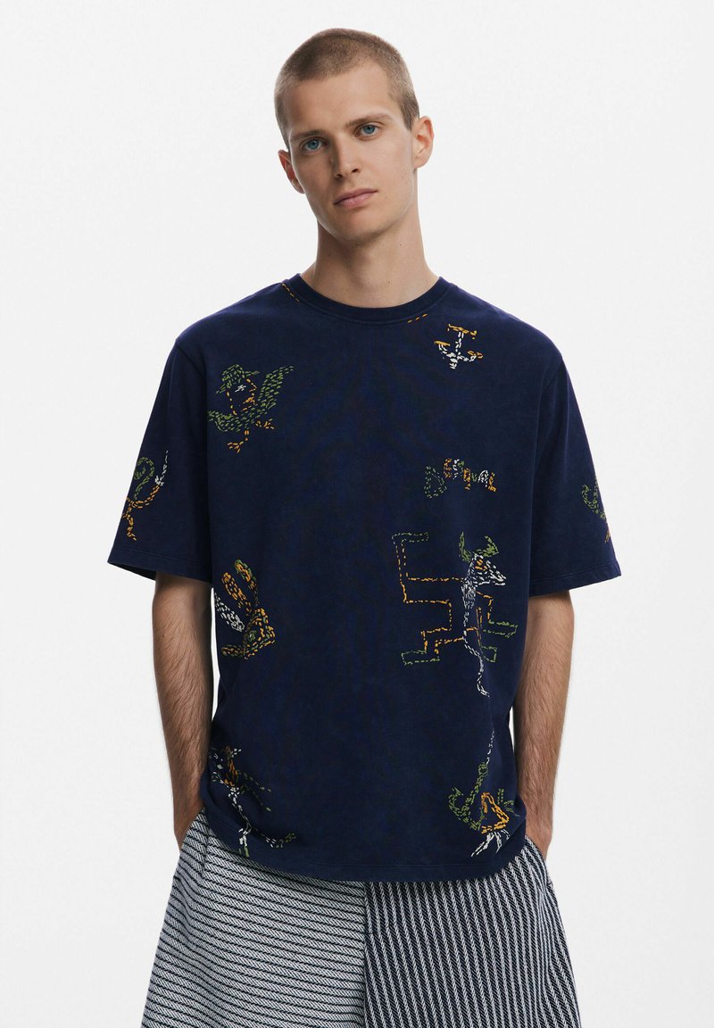 Navyblaues Baumwoll-T-Shirt mit grafischen Mustern in Grün, Orange und Weiß. Lässige Passform, runder Halsausschnitt, kurze Ärmel und weicher Stoff.