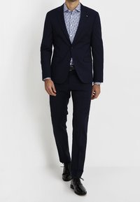 Navy blue tailored suit with a floral patterned shirt underneath. Featuring a single button closure, slim fit pants, and black dress shoes.