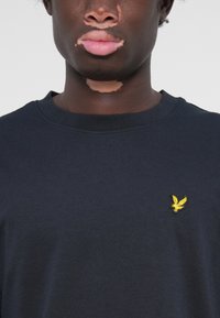 T-shirt en coton bleu marine avec col rond et manches courtes. Présente un petit logo jaune brodé sur la poitrine. Texture douce.