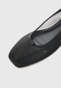 Svarte balletflats med firkantet tå, glatt overmateriale med strukturert overflate, og et tynt, klart nettutsnitt langs kanten.