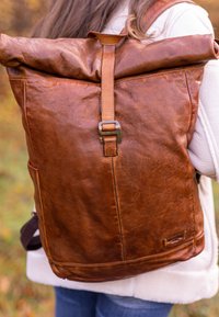 Pruuni nahast rullkott, millel on mati viimistlusega pind, metallist klambri sulgemisega ja ristkülikukujuline kuju. Nähtav tikandi detail.