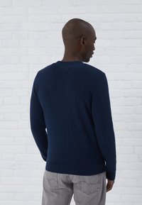 Navyblauwe gebreide trui met lange mouwen, ronde Hals en geribde manchetten en zoom, gecombineerd met lichtgrijze broek.