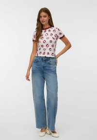 Hvid cropped t-shirt med rødt lip print og rød kant, parret med lyseblå brede jeans. Outfittet har et enkelt design og en afslappet pasform.