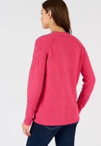 Maglione rosa lavorato a maglia con maniche strutturate e decorate e colletto a costine. Mostrato di spalle, abbinato a jeans in denim scuro.