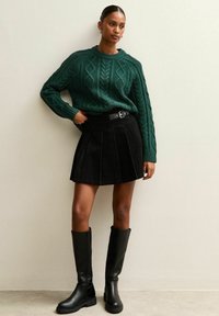 Ciemnozielony sweter z dzianiny w splot kablowy, czarna spódnica z sztruksu z plisami oraz czarne gumowe buty do kolan. Prosty metalowy zamek do paska.