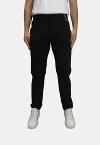 Pantaloni neri con una vestibilità slim, vita elasticizzata e coulisse. Indossati con sneakers bianche, caratterizzate da una texture liscia e senza motivi visibili.