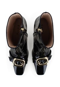 Bottines en cuir verni noir avec un bout pointu, des accents de boucle dorée et des fermetures éclair latérales. L'intérieur présente une doublure beige avec une marque.