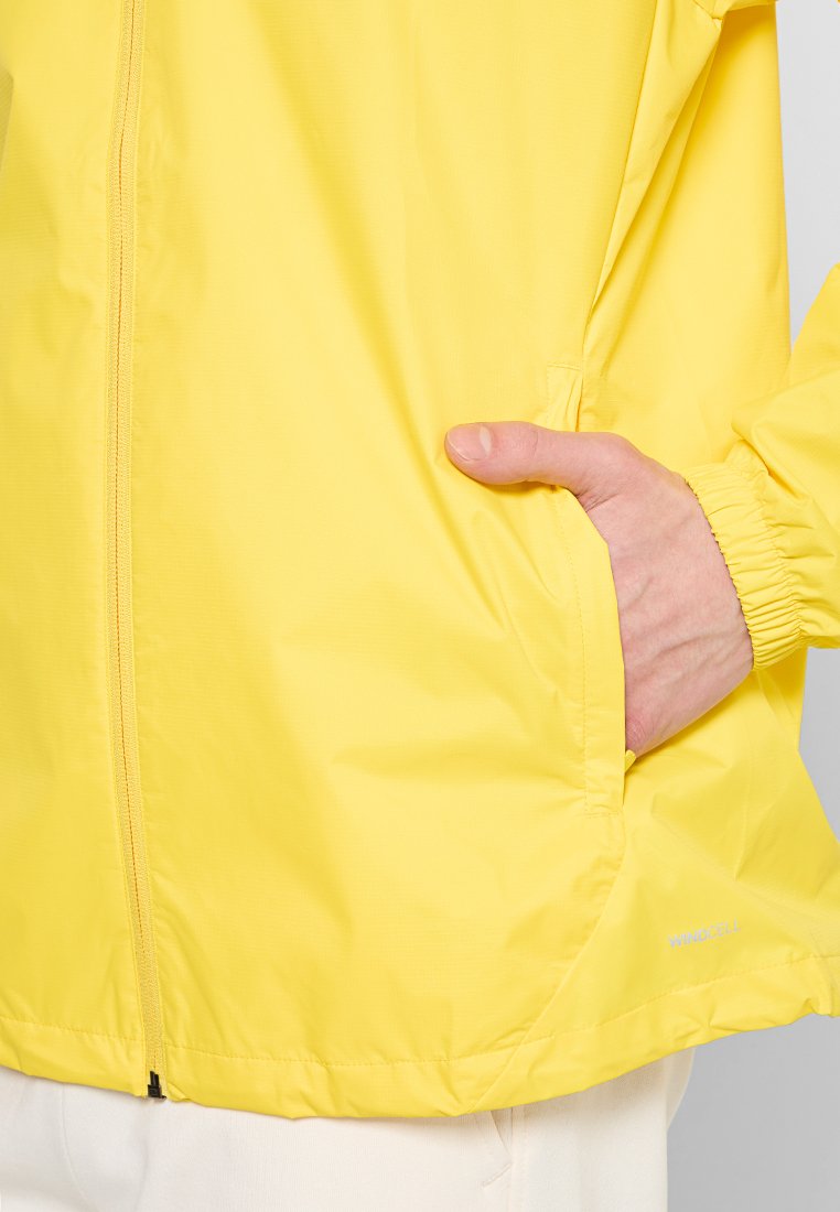 Giacca a vento gialla con zip frontale, polsini elastici e tasche laterali. Tessuto liscio e leggero con una lieve lucentezza.