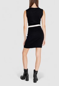 Schwarzes, tailliertes Crop-Top mit kurzen Ärmeln und passendem schwarzem Rock. Weißer Akzent am Bund. Glatte Stricktextur und schlanke Silhouette.