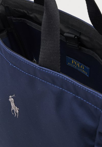 Sac cabas Polo Ralph Lauren bleu foncé avec poignées noires, avec un logo joueur de polo argenté et une étiquette intérieure.