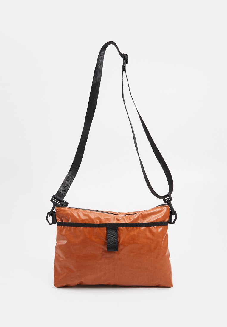 Brown nylon crossbody bag with a black adjustable strap, featuring a zip closure, flat base, and front webbing accent.