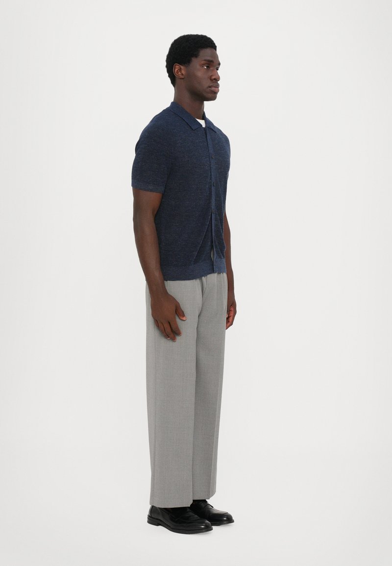 Navy short-sleeve button-up shirt with a textured finish, paired with light gray, pleated trousers and black shoes.