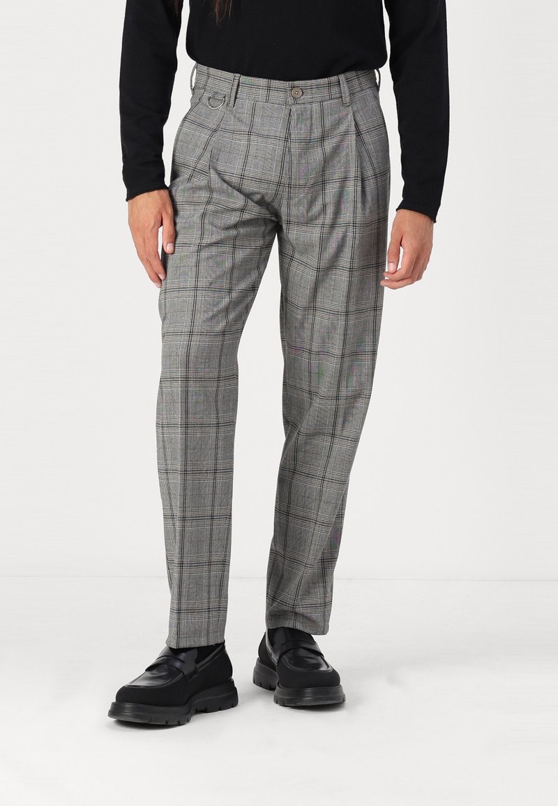 Pantalon à carreaux gris avec une coupe droite, taille haute, plis et poches latérales. Associé à des chaussures noires.