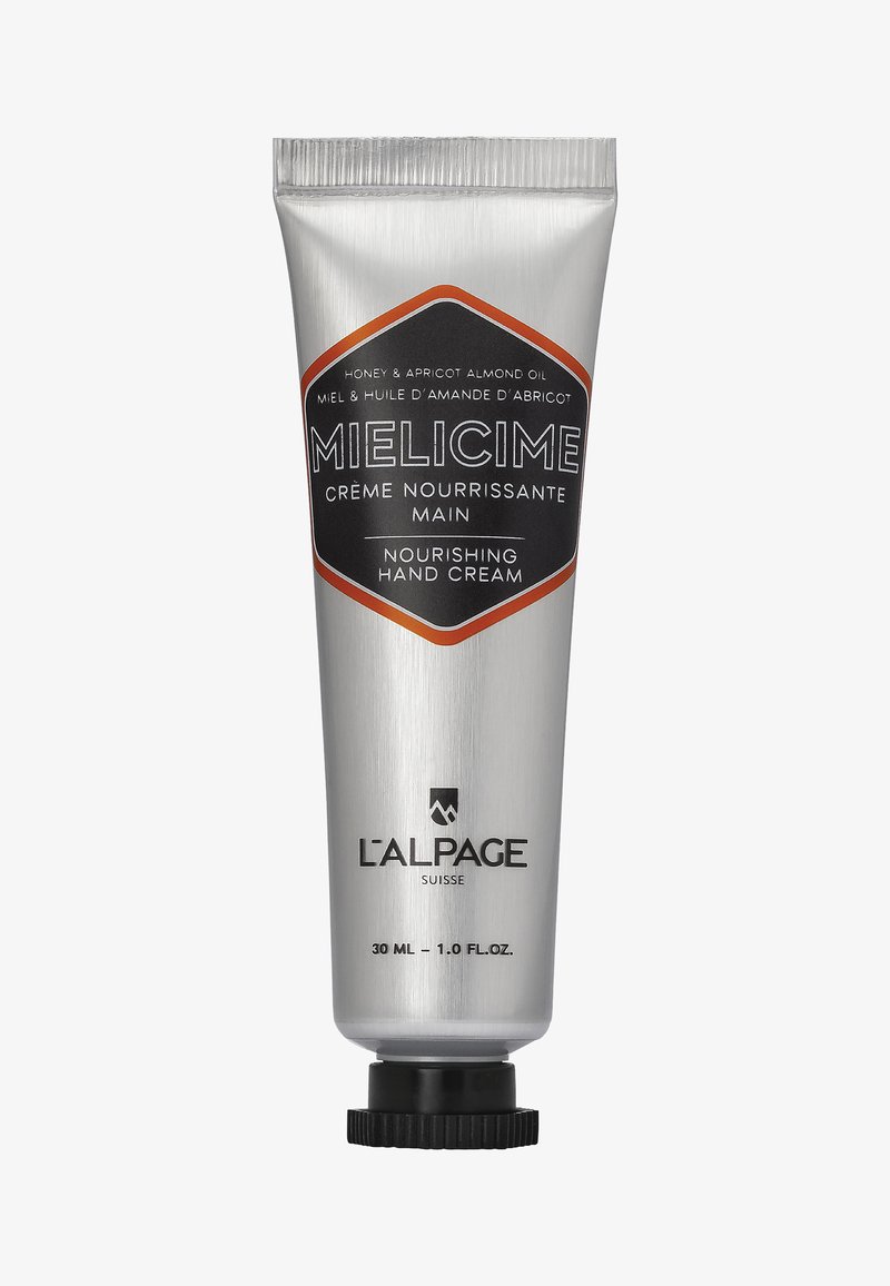 Tube en aluminium de crème pour les mains ; argent avec des accents noirs et orange. Le texte indique "crème pour les mains nourrissante" et les ingrédients clés. Taille de 30 ml.