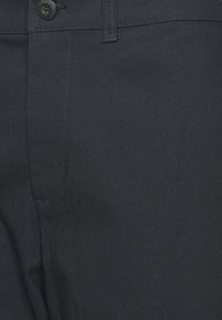 Mörkgrå byxor med en slät textur, försedda med en enda knappstängning, snedställda fickor och diskreta sömmar framtill.