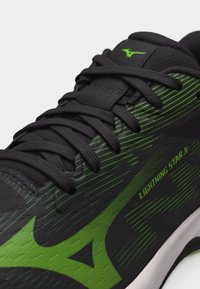 Κοντινή λήψη μαύρου και πράσινου αθλητικού παπουτσιού με μαύρα κορδόνια, κείμενο "LIGHTNING STAR Jr." και πράσινο λογότυπο Mizuno στη γλώσσα και την πλευρά.