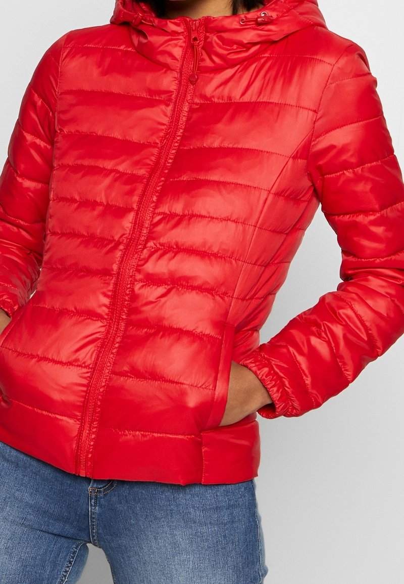 Rote Daunenjacke mit Reißverschluss, Kapuze und gerippten Bündchen. Mit horizontalen Steppnähten und Seitentaschen ausgestattet. Glatte, glänzende Oberfläche.