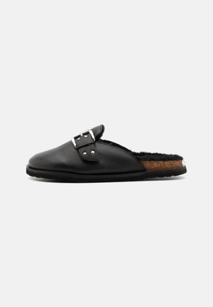 Black leather slip-on shoe with faux fur lining, cork midsole, and silver buckle detail. Flexible rubber outsole for comfort.