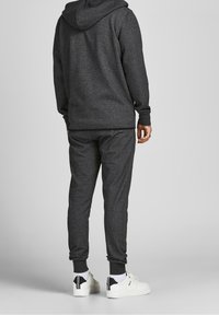 Sudadera gris oscura y pantalones a juego, hechos de un tejido suave. La sudadera tiene un cordón, puños acanalados y dobladillos en los tobillos. Zapatillas blancas.