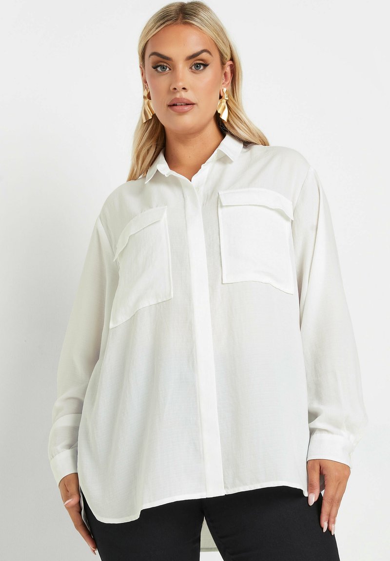 Camicia bianca a maniche lunghe con bottoni, due tasche sul petto, vestibilità rilassata e tessuto leggero e testurizzato. Presenta un colletto.