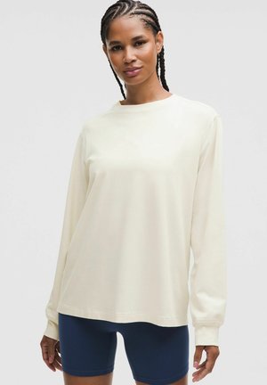 Roomy, crèmekleurige sweatshirt met lange mouwen van zachte stof, met een ronde halslijn en een ontspannen pasvorm, gecombineerd met marineblauwe fietsbroeken.