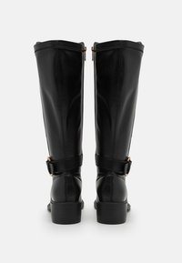 Botas de cuero negro hasta la rodilla con una textura suave, cremalleras laterales, un detalle de hebilla envolvente y un tacón bajo apilado.