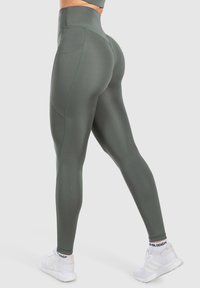 Leggings verts taille haute en tissu évacuant l'humidité avec une texture lisse. Comprend des coutures contrastantes et un design ajusté. Associés à des baskets blanches.