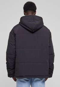 Sort dunjakke med hætte, der har et quiltet design og en afslappet pasform. Struktureret stof med elastiske manchetter og kant.