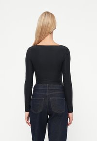 Body noir à manches longues avec un décolleté carré, texture lisse et coupe ajustée. Associé à un jean en denim foncé taille haute.