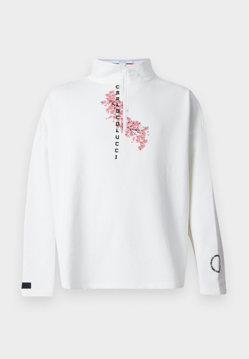 Biały sweter z wysokim kołnierzem i półzamkiem. Ozdobiony różowym haftem przedstawiającym kwiaty wiśni oraz czarnym napisem. Długie rękawy; lewy rękaw ma czarny akcent.