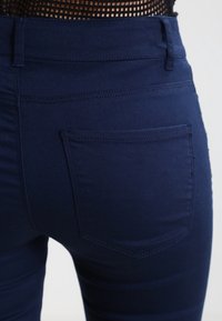 Tummansinisiä puuvillasekoitefarkkuja, joissa on takatasku, jossa on ommeltu reuna, sileä pinta ja slim fit -muotoilu.