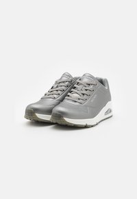 Graue Sportschuhe mit einem glatten synthetischen Obermaterial und perforierten Details. Mit einer weißen Sohle und einer Luftpolstereinheit. Schnürdesign.