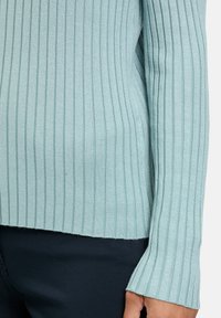 Light blue ribbed sweater with long sleeves, featuring fine texture and a fitted design, hemmed at the bottom with a neat finish.