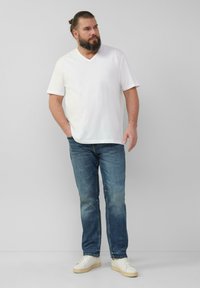 Weißes V-Ausschnitt-T-Shirt, lockere Passform, kombiniert mit blauen Jeans und weißen Sneakers. Lässiges Outfit mit einfachem Design und einfarbigen Farben.