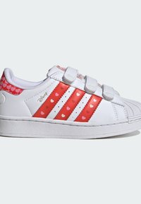 Biele tenisky s červenými akcentmi v tvare srdca, s tromi červenými pruhmi a suchými zipsami, štruktúrovanou gumovou podrážkou a špicatou špičkou.