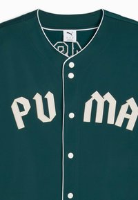 Mėlynos-žalios spalvos beisbolo marškiniai su baltais mygtukais ir kontrastiniu apdailu. Turėkite pakeltą "PUMA" logotipą kreminės spalvos, struktūruotą apykaklę ir audinio tekstūrą.