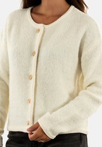 Cardigan in lana color crema con scollatura rotonda, caratterizzato da un orlo intrecciato e sei bottoni dorati sul davanti. Tessuto morbido, vestibilità rilassata.
