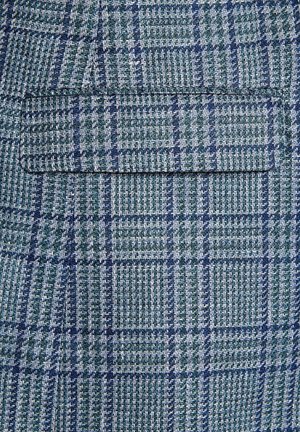 Tkanina tkana w zielono-niebieską kratkę, o fakturze, która wydaje się strukturalna i teksturowana. Zawiera kieszeń naszywaną.