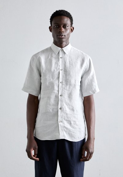Camisa de lino de manga corta, color gris claro, con cuello abotonado, textura sutil y botones en el frente. Combinada con pantalones oscuros de color azul marino.
