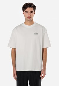 White cotton T-shirt featuring a crew neck, short sleeves, and a small "PEGADOR" logo in black at the left chest. Relaxed fit.