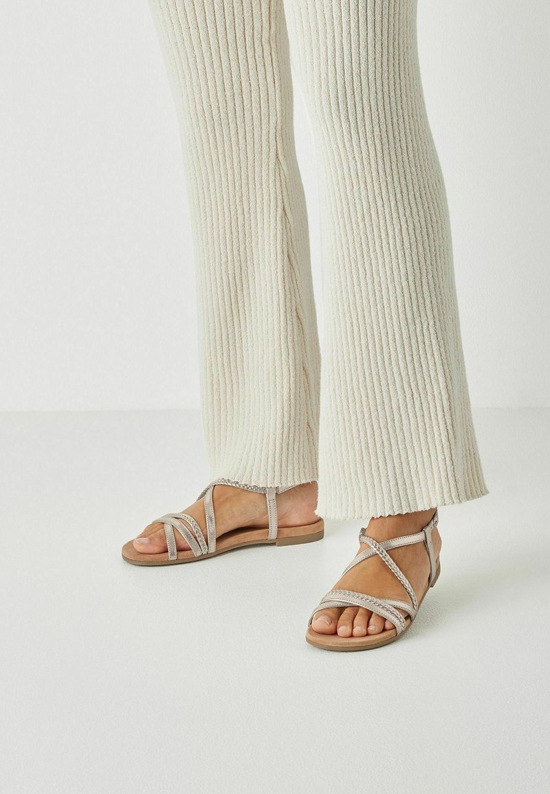 Sandales à bouts ouverts avec plusieurs fines lanières en argent métallique et beige ; semelle plate, avec un accent tissé sur les lanières.