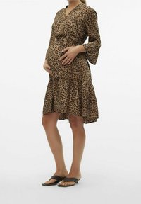 Grön leopardmönstrad gravidklänning med V-halsringning, långa trumpetärmar och vågig fåll. Tillverkad av lättviktsmaterial, kompletteras med platta sandaler.