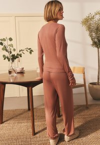 Lätt ribbad loungekläder i dämpade rosa nyanser. Långärmad topp med rundad nederkant, i kombination med matchande tapered byxor. Mjuk tygkänsla.