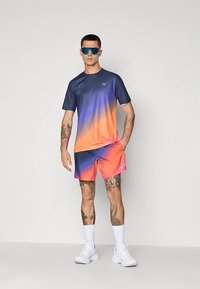 Miesten urheiluasu, jossa on sinisestä oranssiin liukuva lyhythihainen paita ja sitä vastaavat shortsit, valkoiset sukat ja kengät. Huomattava tuotemerkki.