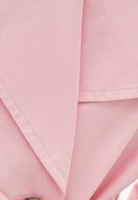 Pink fabric with a smooth texture, featuring folded sections and visible seams. A button is included at the bottom edge.