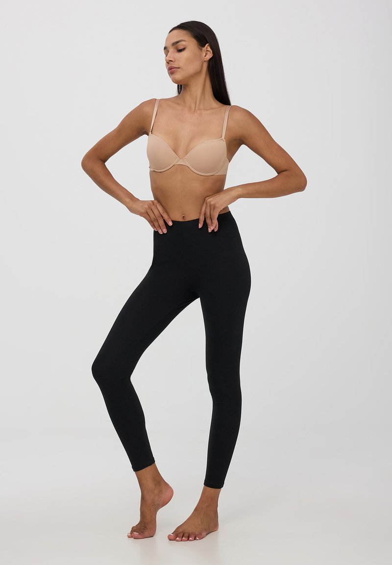 Scollo in beige con coppe imbottite, abbinato a leggings neri a vita alta, realizzati in tessuto elasticizzato, aderenti alla caviglia, design minimal.